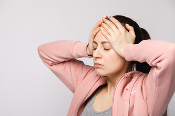 A young woman in a pink tracksuit holds her head with both hands . Suffer from a headache, ache, or pain. I need some medicine to relieve it.