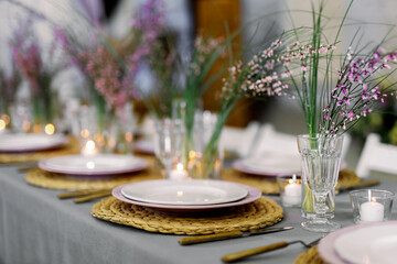 Decorated table ready for dinner. Beautifully decorated table set with flowers, candles, plates and serviettes for wedding or another event in the restaurant. Red and rose flowers on grass.