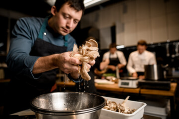 man chef holds oyster mushrooms over bowl on kitchen - obrazy, fototapety, plakaty