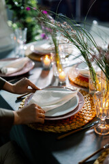 Table decorated with genista flowers and bergrass. Serving with wicker coasters for plates, napkins, burning candles and glasses. Decorations and table for wedding and dinner parties.