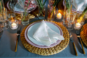 Table decorated with genista flowers and bergrass. Serving with wicker coasters for plates, napkins, burning candles and glasses. Decorations and table for wedding and dinner parties.