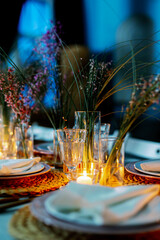 Table decorated with genista flowers and bergrass. Serving with wicker coasters for plates, napkins, burning candles and glasses. Decorations and table for wedding and dinner parties.