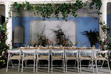 Table decorated with genista flowers and bergrass. Serving with wicker coasters for plates, napkins, burning candles and glasses. Decorations and table for wedding and dinner parties.