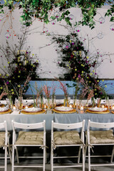 Table decorated with genista flowers and bergrass. Serving with wicker coasters for plates, napkins, burning candles and glasses. Decorations and table for wedding and dinner parties.