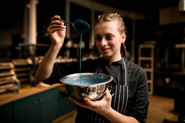 smiling female chef holds bowl with blue sauce and pours it with spoon