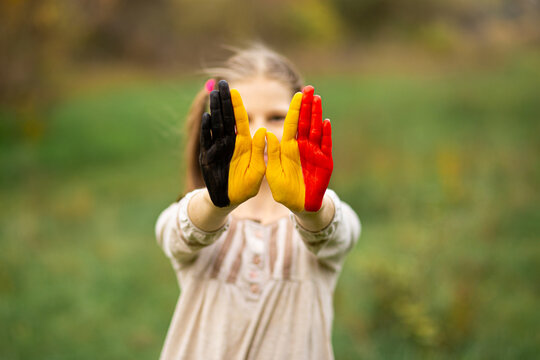 Child girl show hands painted in Belgium flag colors walking outdoor, focus on hands