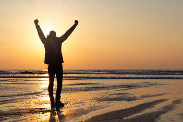 Silhouette of man on beach at sunset with sunburst cornwall England uk