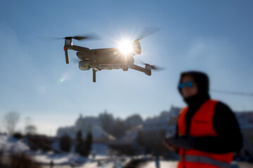 Close up picture of flaying quadrocopter dron and pilot siluette in sunset light and blue sky background, Man flying a drone in the city using a controller, © wip-studio