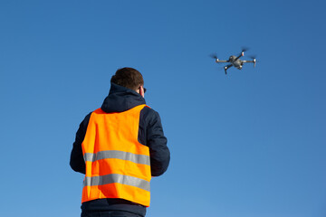 Close up picture of flaying quadrocopter dron and pilot siluette in sunset light and blue sky background, Man flying a drone in the city using a controller,