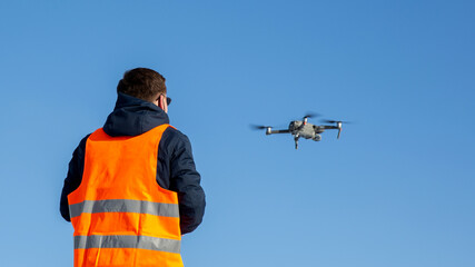 Close up picture of flaying quadrocopter dron and pilot siluette in sunset light and blue sky background, Man flying a drone in the city using a controller, © wip-studio