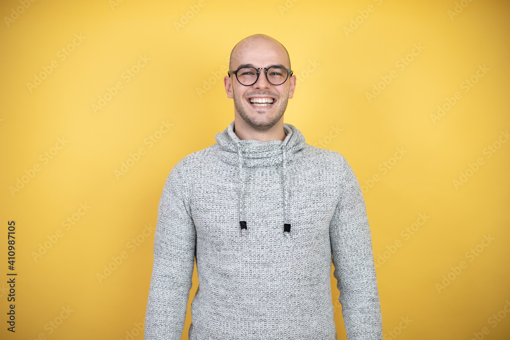 Wall mural Young bald man wearing glasses over yellow background