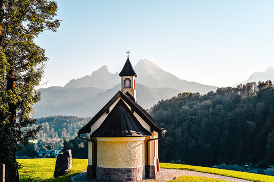 Amazing alpine panorama with the Kirchleitn chapel in the front and the the huge Watzmann mountain in the background under a clear blue sky.