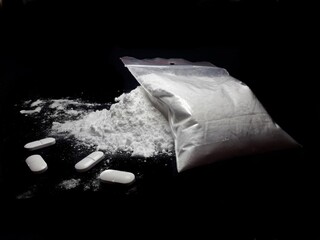 Cocaine drug powder pile ang bag and pills on black background