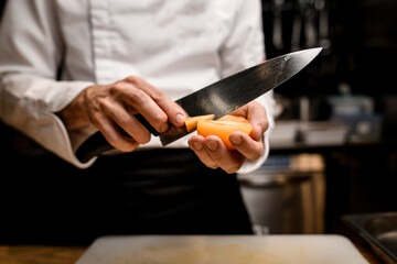 close-up view of yellow tomato in hand of chef which cuts with knife