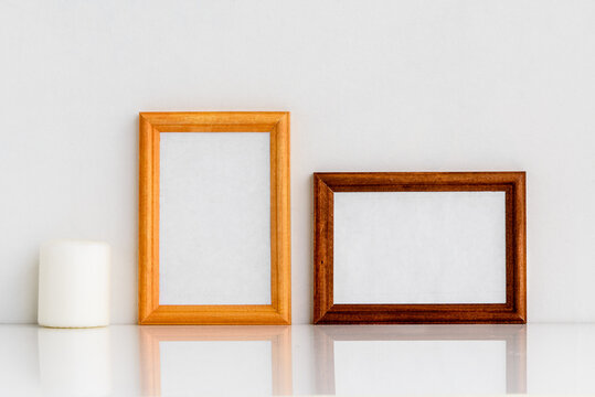 Two wooden frames with a white insert inside and a white decorative candle. Photo frame on a white wall background.