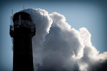 Large chimney with clouds of smoke against the sky.