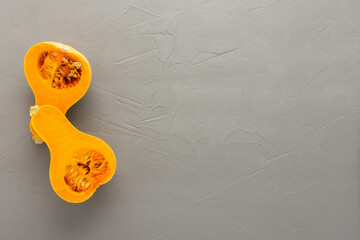 Raw organic butternut pumpkin or gramma cut in half close-up on gray concrete background, top view, copy spase
