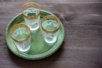 Aerial view of three empty glasses of Arab tea on a green tray, on a rustic wooden table, horizontally, with copy space