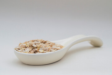 Ceramic white spoon with flakes of various cereals on a white background.