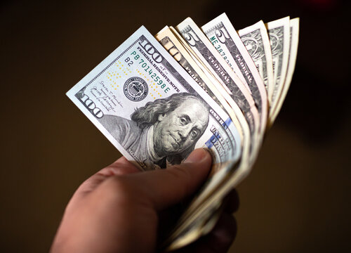 Money, Us dollars ( USD ). A man holding dollar bills in hand whith dark background. Finance, business, investment and income concept.