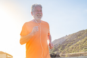 old man or senior running alone in a rural zone around the nature and houses - one mature male doing exercise and losing weight