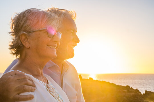 Couple Of Two Cute Seniors Together Enjoying Summer And Having Fun At The Beach Looking At The Sea Or Ocean With Sunset - Mature People Having A Good Lifestyle