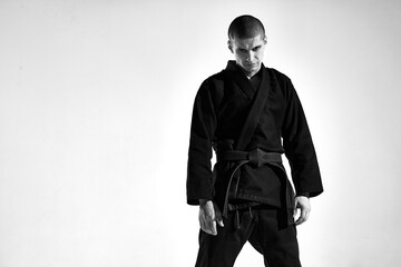 Confident frowning aggressive guy in kimono for mix fight on studio background with copy space, black and white portrait