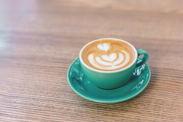 Cup of cappuccino with latte art on wooden background.