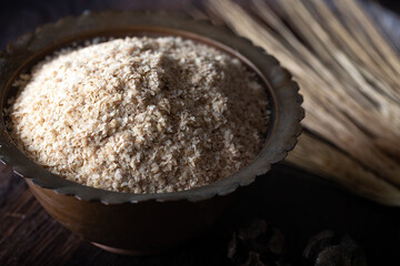 Raw wheat germ in the metal bowl on wooden background. Wheat germ in bowl in front of a dark background. 
