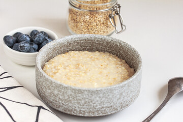 Healthy breakfast oatmeal porridge in bowl, blueberries and jar of steel cut oats on grey background. Steel cut oats, vegan vegetarian weight loss dieting breakfast