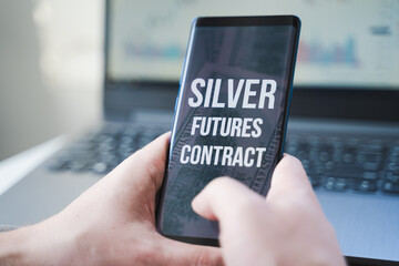 Mobile phone with text: silver futures contract and money, dollars in hand. Financial trading. Investment in precious metals. Playing on stock exchange, market manipulation.Losses, crisis.Short float