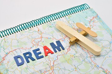 Fototapeta na wymiar La palabra dream y un avión hecho con una pinza y palos de polos sobre un mapa