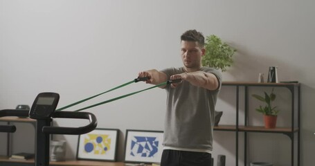 handsome man is doing exercises with sport rubber band in apartment, stretching tape and tensing muscles