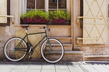 The bicycle stands near a vintage wall with a window and shutters.	