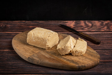 Halva, also halvah or halwa, West Asia sweet dessert made of sesame oily seeds grinded to a paste and mixed with sugar syrup served and sliced on cutting board on dark wooden table with knife