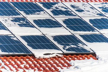 Solar photovoltaic panels PV on a snowy house roof, blue sky with copy space. - 411006103