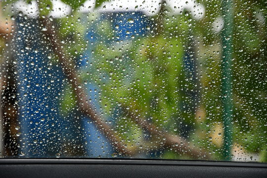 Car door with wet glass window covered by raindrop bubbles from behind. Transparent surface with rain drops shot from inside automobile. Abstract blurred background