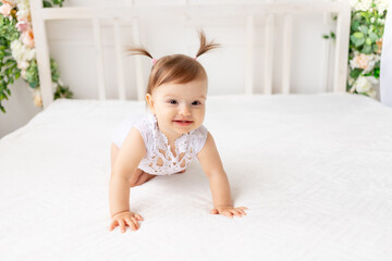 funny baby girl six months crawling in a bright beautiful room on a white bed in a lace bodysuit and smiling