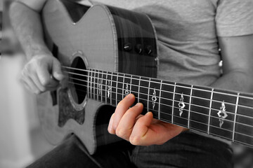 Fototapeta na wymiar Guitarist playing an acoustic guitar with the focus on his fingers. Selective color of fingers on a black and white picture.
