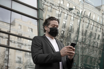 businessman talking on the phone. Caucasian man in blazer and mask with cell phone in hand in front of glass building   