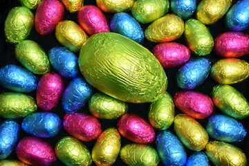 Pile or group of multi colored and different sizes of colourful foil wrapped chocolate easter eggs in pink, blue, yellow and lime green with a large green egg in the middle.