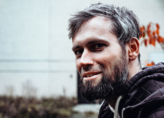 Smiling handsome young or a middle-aged Caucasian man portraited in the city, with white skin, grey and black hair having a friendly and confident look on his face. Background with fall moody colours 