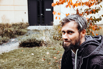 Smiling handsome young or a middle-aged Caucasian man portraited in the city, with white skin, grey and black hair having a friendly and confident look on his face. Background with fall moody colours 