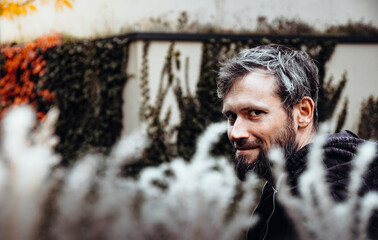 Artistic photo portrait confident smiling handsome middle-aged Caucasian man portraited in the city, with white skin, grey and black hair having a friendly look on his face, wearing a blue jacket.