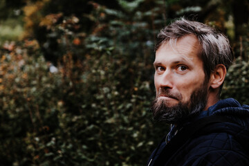 Portrait of a handsome bearded young or middle-aged Caucasian man, wearing a blue jacket, with white skin and grey hair having surprised look on his face. Background with fall moody colours.