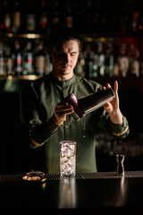 crystal glass with ice cubes stands on the bar counter and male bartender in background