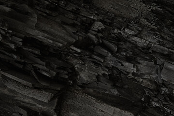 Black, dark aged shabby cliff face, divided by huge cracks, tectonics layers. Coarse, rough gray stone, rock texture of mountains, background, copy space for text on theme geology, mountaineering.