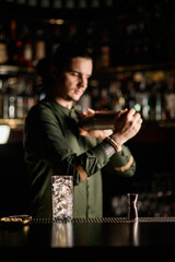transparent glass with ice and jigger stand on bar counter. Blurred bartender in background