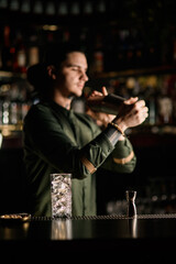 glass with ice and jigger stand on bar counter. Blurred bartender in background