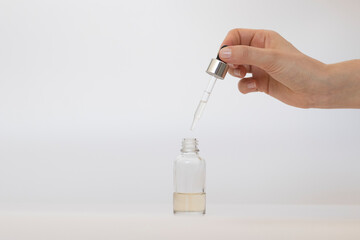 Hand holding a dropper from a glass bottle over a white background